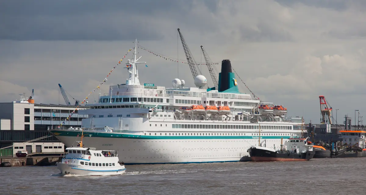 Das weiße Kreuzfahrtschiff Albatros liegt im Hafen von Bremerhaven, während kleine Boote auf dem Wasser fahren.