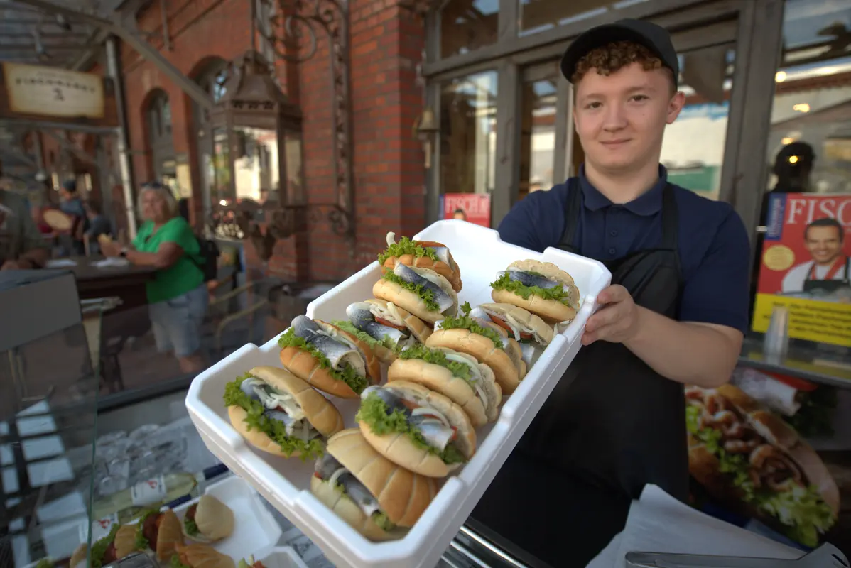 Ein junger Verkäufer in Bremerhaven präsentiert ein Tablett voller frischer Fischbrötchen.