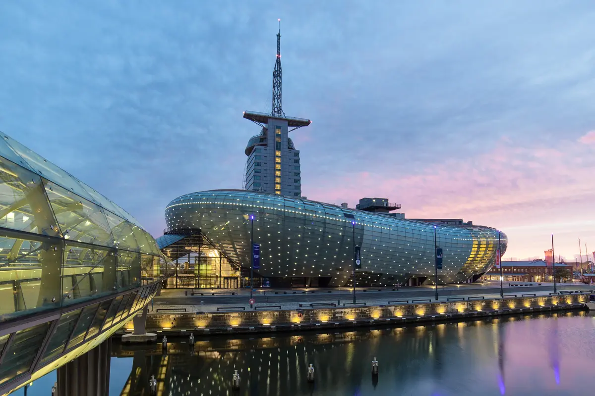 Aussenansicht des beleuchteten Klimahauses in Bremerhaven zur Blauen Stunde mit Wasserspiegelung.