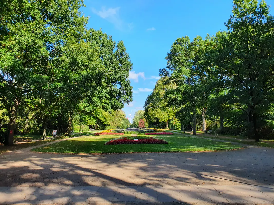 Ein sonniger Park mit grünen Bäumen, gepflegten Rasenflächen und bunt bepflanzten Blumenbeeten im Bürgerpark Bremerhaven.