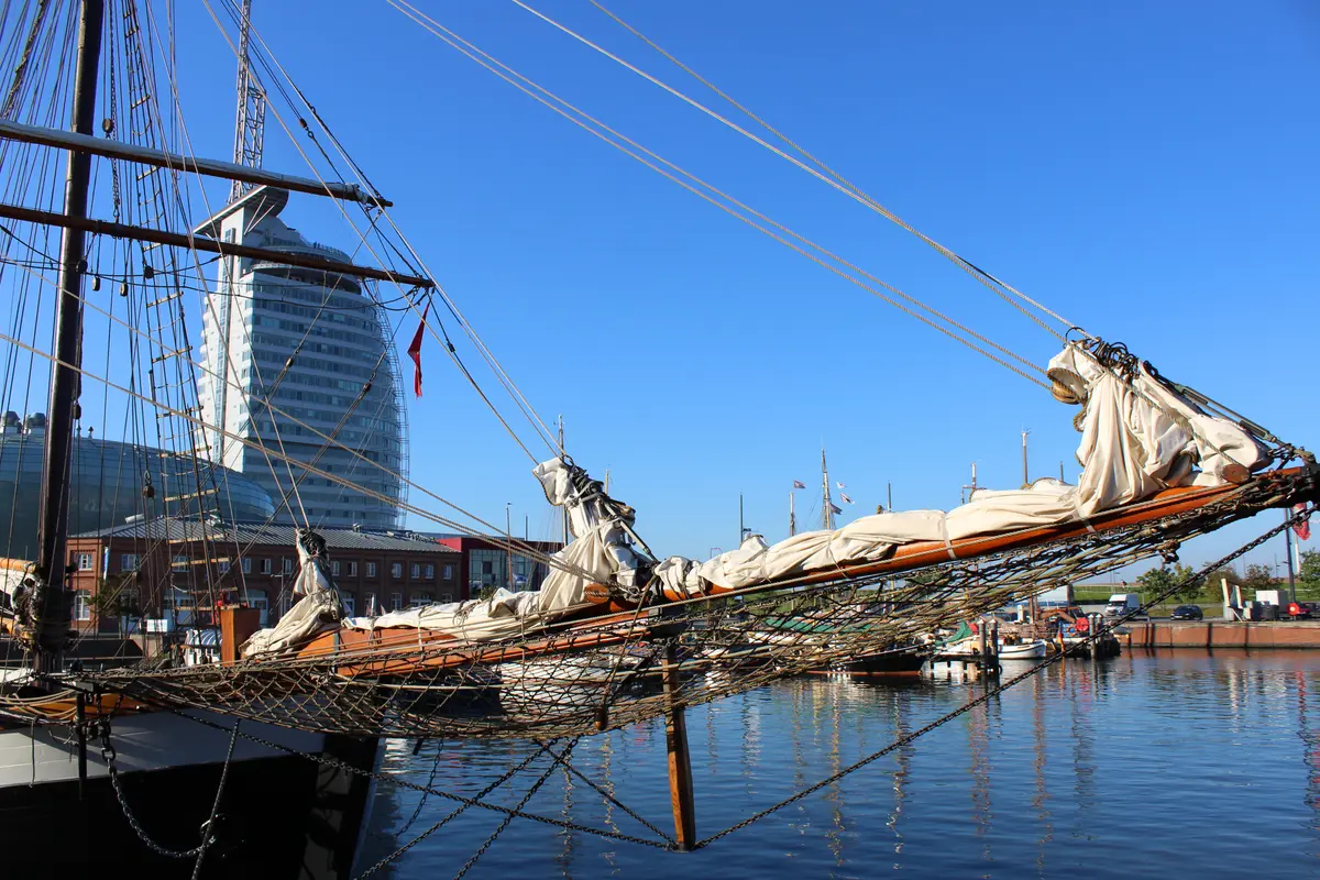 Der hölzerne Klüverbaum eines historischen Segelschiffs im Hafen von Bremerhaven vor dem modern gestalteten Atlantic Hotel Sail City.