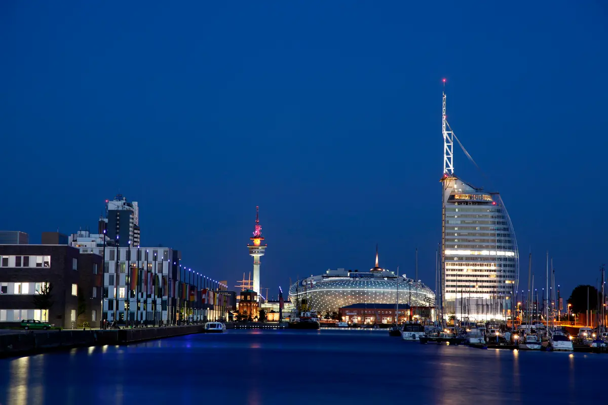 Beleuchtete Skyline der Havenwelten in Bremerhaven zur Blauen Stunde mit Blick über das Wasser des Neuen Hafens.