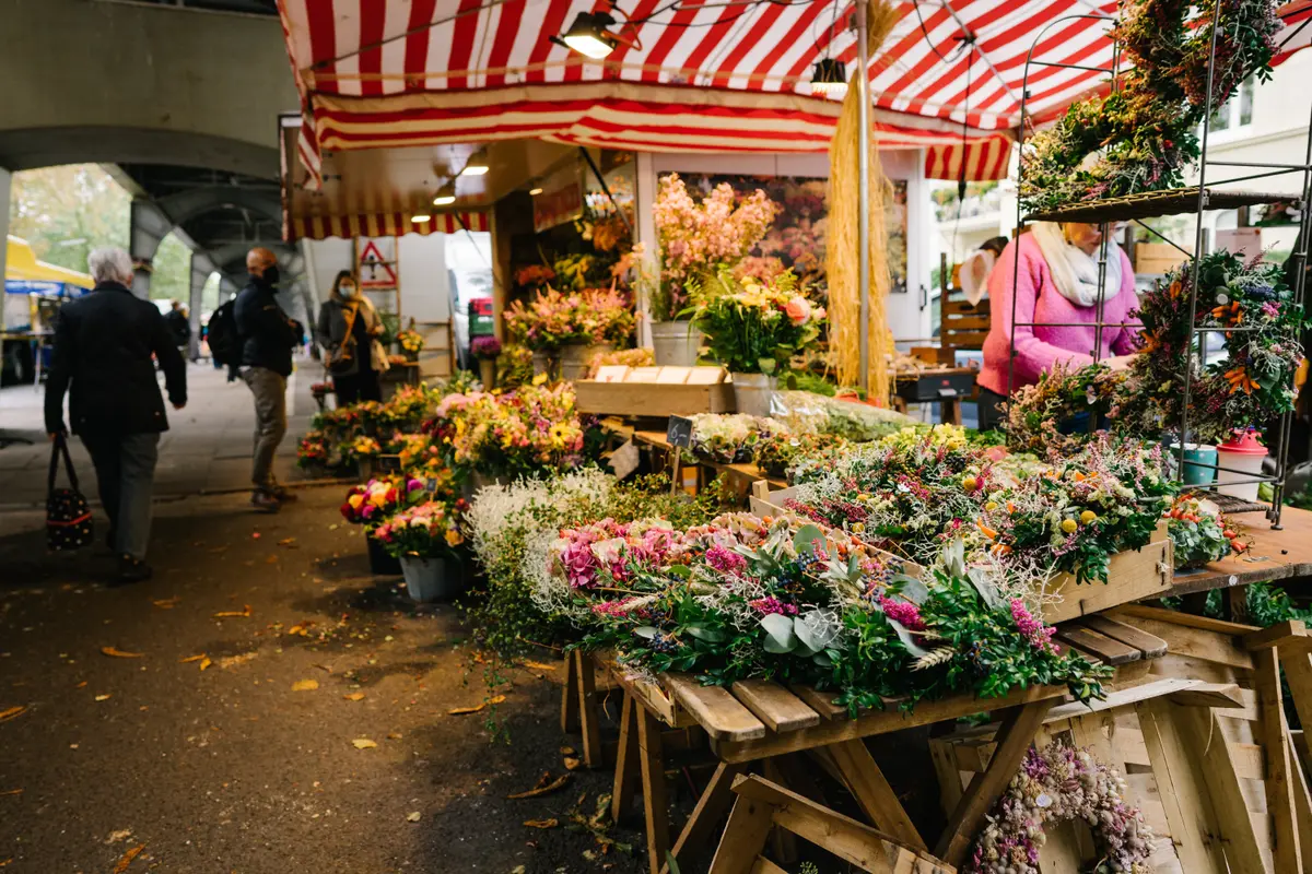 Ein bunt geschmückter Blumenstand mit frischen Pflanzengestecken auf einem überdachten Wochenmarkt in Hamburg.