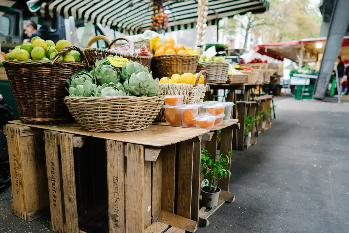 Holzkisten und Flechtkörbe voller Artischocken, Zitronen und Limetten auf einem Wochenmarkt in Hamburg.