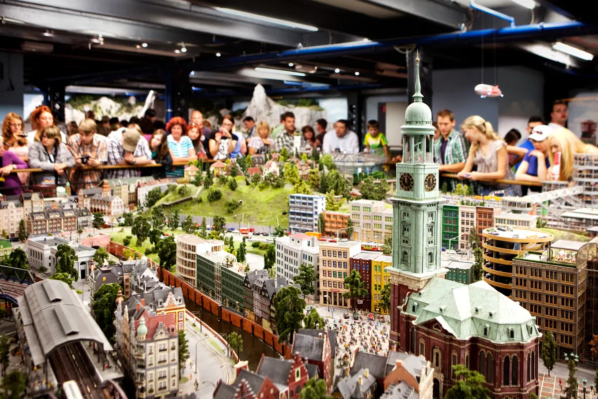 Blick auf das Miniatur Wunderland in Hamburg mit dem Modell des Hamburger Michels und vielen Besuchern im Hintergrund.