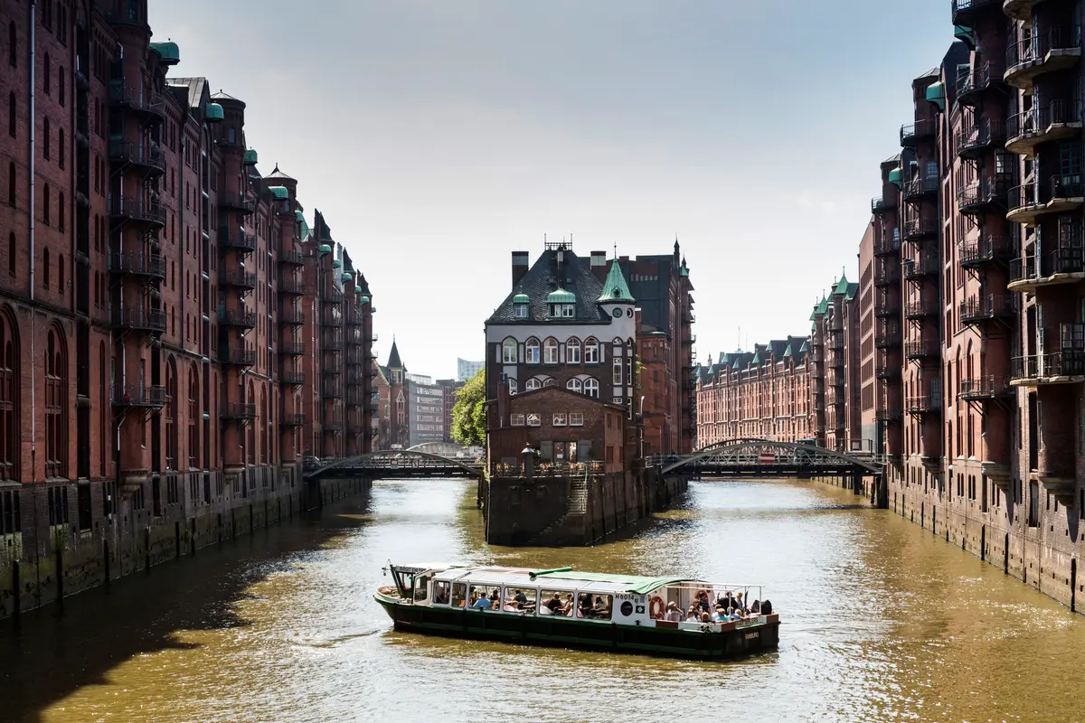 Blick auf das Wasserschloss in der Hamburger Speicherstadt mit historischen Backsteinbauten und einem Ausflugsschiff auf dem Wasser.