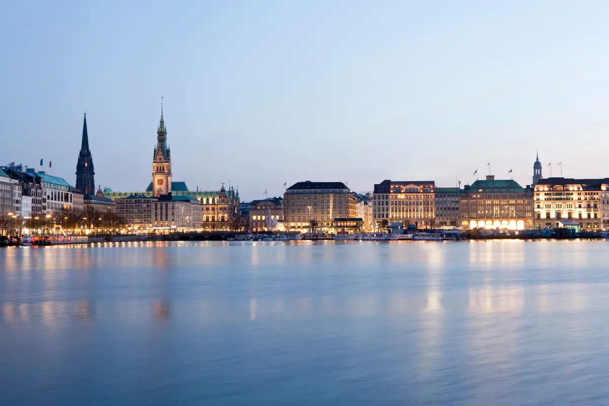 Blick über die ruhige Binnenalster in Hamburg auf die beleuchtete Skyline mit dem Rathausturm zur blauen Stunde.