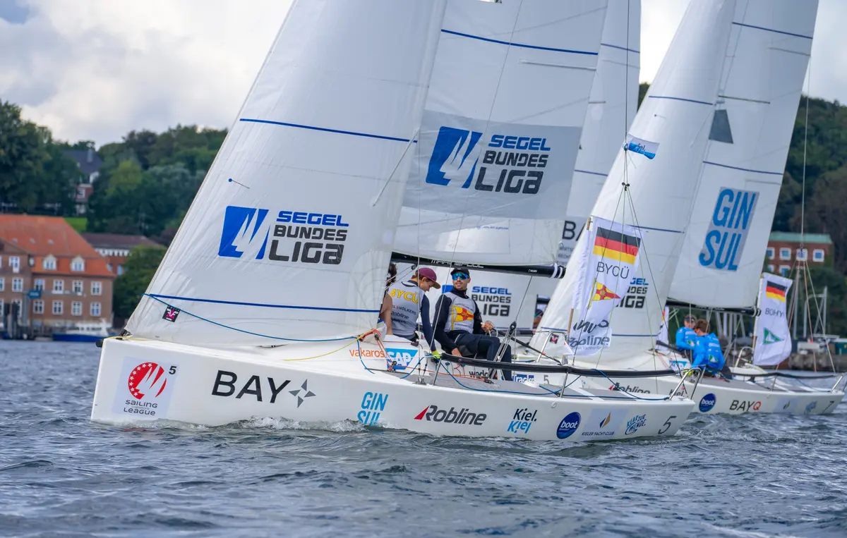 Segelboote mit Crew-Mitgliedern liefern sich ein spannendes Regatta-Rennen auf dem Wasser in Kiel.