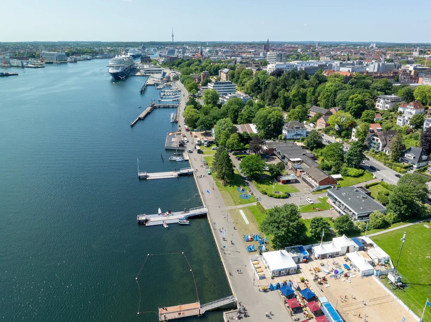 Luftbild der Kiellinie in Kiel mit der Uferpromenade, Stegen und einem Kreuzfahrtschiff im Hintergrund.