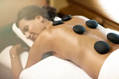 Eine entspannte Frau lächelt auf einer Massageliege, während mehrere heiße Steine auf ihrem nackten Rücken liegen.