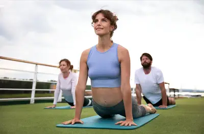 Drei Menschen machen Yoga auf dem Sonnendeck eines Flussschiffs. Die Frau im Vordergrund führt eine Upward-Facing Dog Pose aus.