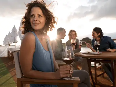 Eine Gruppe von vier Personen genießt Wein auf dem sonnigen Deck eines Flusskreuzfahrtschiffs. Eine Frau im Vordergrund blickt lächelnd in die Ferne.