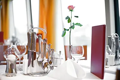 Ein elegant gedeckter Restauranttisch mit Besteck, Gläsern, Serviette, roter Menükarte und einer rosa Rose als Dekoration.