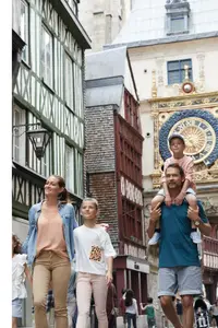 Familie mit Kindern spaziert durch die Altstadt von Rouen, mit Fachwerkhäusern und der astronomischen Uhr Gros-Horloge im Hintergrund.