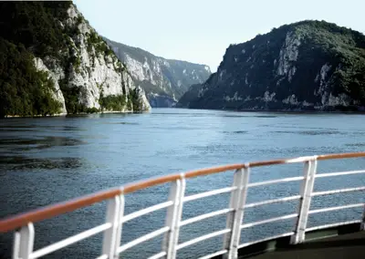 Blick von einem Flusskreuzfahrtschiff auf die imposante Felslandschaft der Donau bei den Katarakten mit bewaldeten Hängen und blauem Wasser.