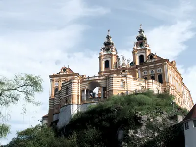 Blick auf das barocke Stift Melk in Österreich mit seinen charakteristischen gelb-weißen Fassaden und zwei hohen Türmen auf einem grünen Hügel.