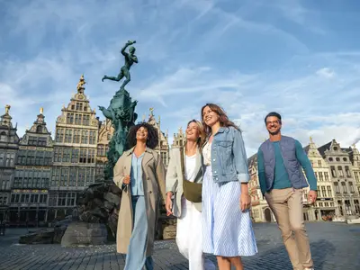 Vier lachende Menschen spazieren durch Antwerpen, im Hintergrund sind historische Gebäude und der Brabo-Brunnen zu sehen.