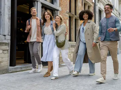 Fünf lachende Freunde spazieren durch eine historische Gasse in Antwerpen, genießen den Stadtbummel bei Tageslicht.