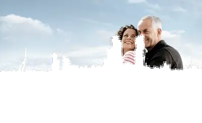 Lächelndes Paar auf einem Schiffsdeck mit Blick auf die beeindruckende Skyline von Rotterdam und die Erasmusbrücke unter blauem Himmel.