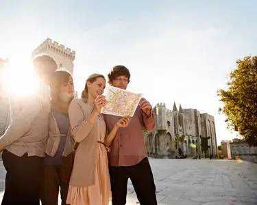 Vier Touristen in Avignon schauen bei Sonnenuntergang vor einem historischen Palais gemeinsam auf einen Stadtplan.