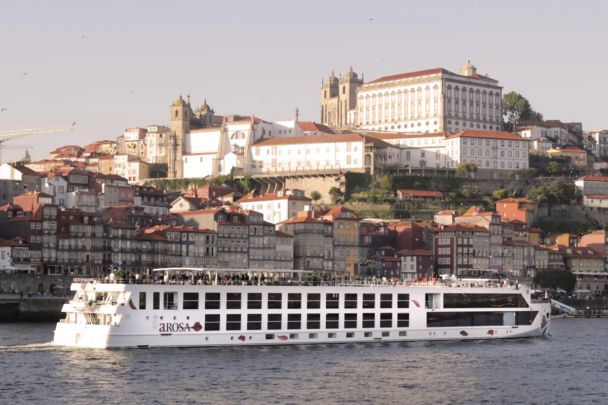 Das Flusskreuzfahrtschiff A-ROSA ALVA fährt auf dem Douro entlang der historischen Uferpromenade von Porto mit bunten Häusern und Kathedralen.