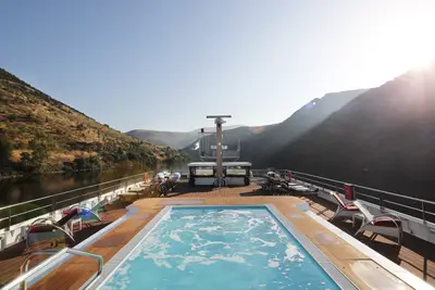 Ein sprudelnder Whirlpool auf dem Sonnendeck der A-ROSA ALVA, umgeben von Bergen und einem Fluss unter klarem Himmel am Morgen.