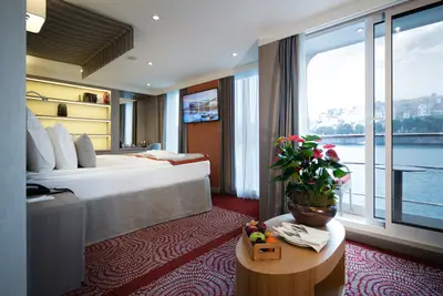 Modern eingerichtete Suite auf der A-ROSA ALVA mit Doppelbett, stilvollem Interieur und Balkon mit Flussblick bei Tageslicht.