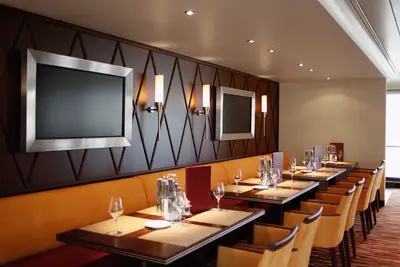 Ein stilvoll eingerichteter Restaurantbereich an Bord der A-ROSA Aqua mit dunklen Wänden, orangefarbenen Sitzbänken und eingedeckten Tischen.