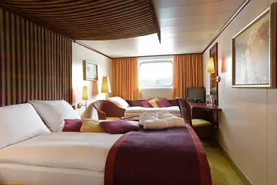 Gemütliche Aussenkabine auf der A-ROSA BELLA mit Doppelbett, Tagesbett, Fenster und Schreibtisch, warm beleuchtet.