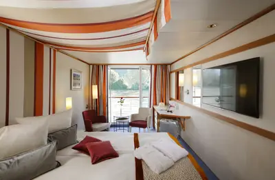 Helle Flusskreuzfahrt-Kabine der A-ROSA DONNA mit Doppelbett, roter Bettwäsche, Schreibtisch, TV und offenem französischen Balkon mit Flussblick.