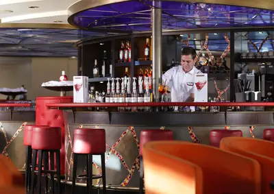 Blick in die Bar der A-ROSA DONNA mit roter Einrichtung und einem Barkeeper, der Cocktails zubereitet.