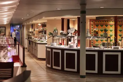 Blick auf den Buffetbereich eines A-ROSA Schiffes mit Koch und vielfältiger Speisenauswahl. Im Hintergrund ein Restaurantbereich mit weiteren Tischen.