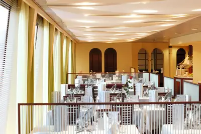 Innenansicht eines eleganten Restaurantbereichs auf einem Flussschiff mit vielen gedeckten Tischen und hellen Panoramafenstern.