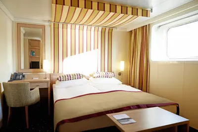 Helle Aussenkabine auf der A-ROSA FLORA mit Doppelbett, Fenster, Schreibtisch und gestreiften Vorhängen in Gelb und Rot.