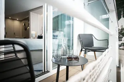 Moderner Balkon einer A-ROSA SENA Flusskreuzfahrtkabine mit Tisch, Stühlen und Blick auf Fluss und Landschaft. 
