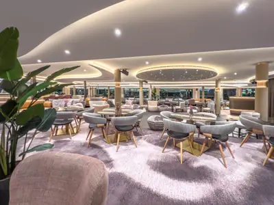 Geräumige, modern eingerichtete Lounge auf einem A-ROSA Flussschiff mit bequemen Sesseln, Tischen und stimmungsvoller Deckenbeleuchtung.