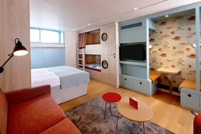 Helle, modern eingerichtete Familienkabine mit Doppelbett, Etagenbetten, integriertem TV und einem gemütlichen Sitzbereich mit Meerestier-Tapete.