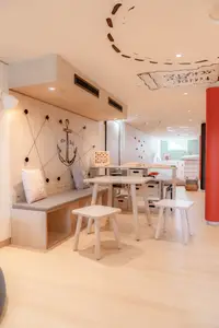 Heller Kids Club mit Holzbänken, Tischen, Stühlen und einem Anker-Motiv an der Wand sowie einer Schatzkarte an der Decke.