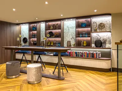 Blick in die helle Connect Lounge auf dem A-ROSA SENA, mit langer Holztheke, Hockern, eleganten Regalen und Büchern.