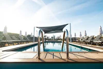 Ein Pool auf dem Sonnendeck der A-ROSA SENA, umgeben von Liegestühlen und Sonnenschirmen unter blauem Himmel bei Sonnenaufgang.