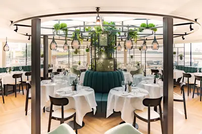 Helles, modernes Restaurant auf der A-ROSA SENA mit elegant gedeckten Tischen, grünen Pflanzen und Flussblick durch große Fenster.