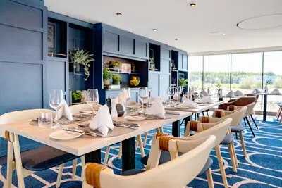 Modernes Restaurant auf der A-ROSA SENA. Elegant gedeckte Tische, blaue Akzente und weite Sicht auf die Flusslandschaft durch Panoramafenster.