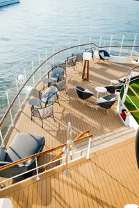 Vogelperspektive auf das vordere Sonnendeck der A-ROSA SENA mit modernen Lounge-Möbeln und dem Rhein im Hintergrund. Eine Schiffsglocke ist im Vordergrund sichtbar.