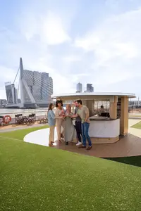 Fünf Personen stoßen an der Up & Down Bar auf dem Sonnendeck eines A-ROSA Flussschiffes an. Im Hintergrund ist eine moderne Skyline mit Brücke zu sehen.
