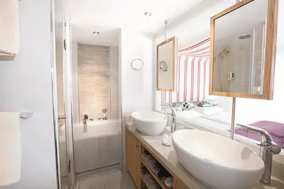 Modernes Bad in einer A-ROSA SILVA Suite mit Doppelwaschbecken, Badewanne, Dusche und Spiegeln zum Schlafbereich.