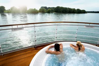 Zwei Personen im Whirlpool auf dem Deck der A-ROSA VIVA genießen den Ausblick auf den Fluss bei Sonnenschein.