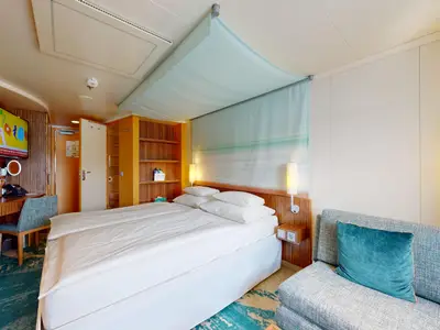Innenansicht einer geräumigen Meerblickkabine an Bord der AIDAbella. Sie zeigt ein grosses Doppelbett, einen Schreibtisch mit Stuhl, einen Fernseher, ein Sofa mit Kissen und eine helle, moderne Einrichtung.