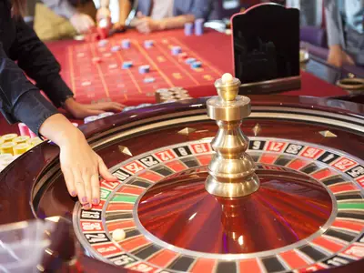 Nahaufnahme einer Person, die am Roulette-Rad im Casino an Bord der AIDAbella spielt. Die Kugel dreht sich, im Hintergrund sind weitere Spielchips und der Spieltisch zu sehen.