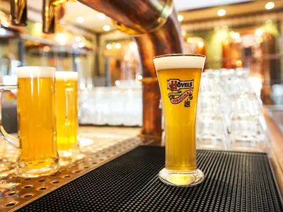 Drei Gläser frisch gezapftes Hövels Original Bier stehen auf einer Theke im Brauhaus an Bord der AIDAblu. Zwei Zapfhähne sind im Hintergrund sichtbar.