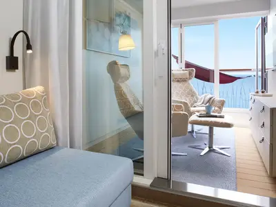 Eine helle, modern eingerichtete Verandakabine an Bord der AIDAcosma mit Sessel, Couch und Meerblick. Auf dem Balkon ist eine rote Hängematte zu sehen.
